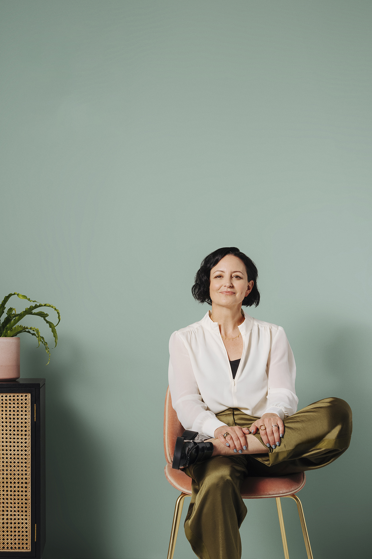 woman sat next to side cabinet in front of green wall