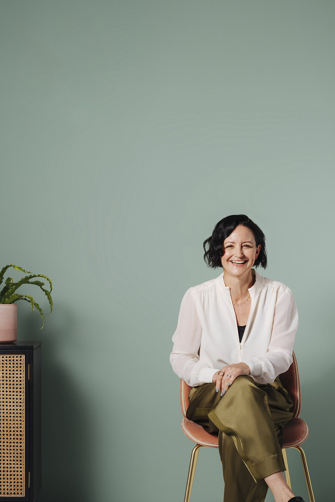 woman sat next to side cabinet in front of green wall